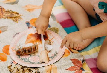 Detailaufahme, ein Kind sitz auf einer Picknickdecke und schneidet eine Bratwurst