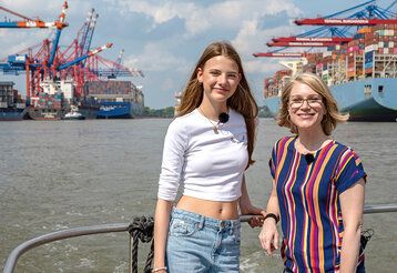 zwei Mädchen auf einem Schiff im Hamburger Hafen, im Hintergrund Hafenanlage und Containerschiff