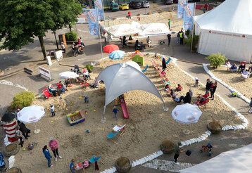 Veranstaltungsort, aufgeschütteter Sand, Pavillon, Zelt, Sonnenschirme Besucher von oben fotografiert