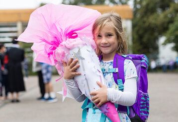 Ein Mädchen steht auf einem Schulhof und hält stolz eine rosa Schultüte im Arm