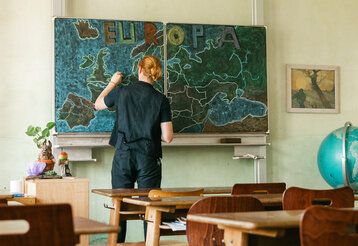 Ein Lehrer steht in einem Klassenzimmer und zeichnet eine Europa-Karte an die Tafel