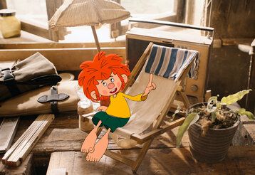 Zeichentrickfigur Pumuckl sitz auf einem kleinen Klapp-Liegestuhl in Meister Eders Werkstatt