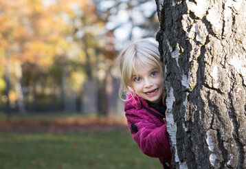 Kleines Mädchen schaut frech hinter Baum hervor