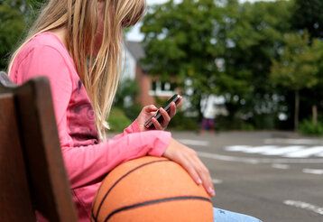 Junges Mädchen sitzt auf einer Bank und nutzt Smartphone
